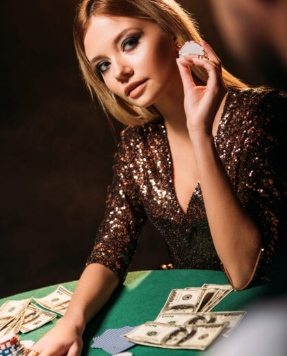 attractive girl holding poker chip and looking at croupier at casino